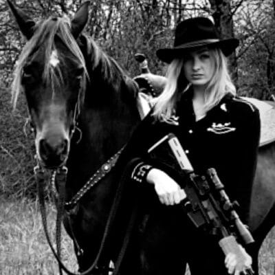 student standing with gun in hand next to horse
