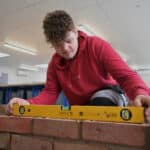 Stratford-upon-Avon College construction brick laying student uses a spirit level on brickwork.