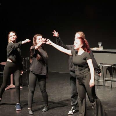 Stratford College actors, clinking imaginary glasses during a performance