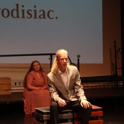 Man sitting on stool singing a song under spotlight