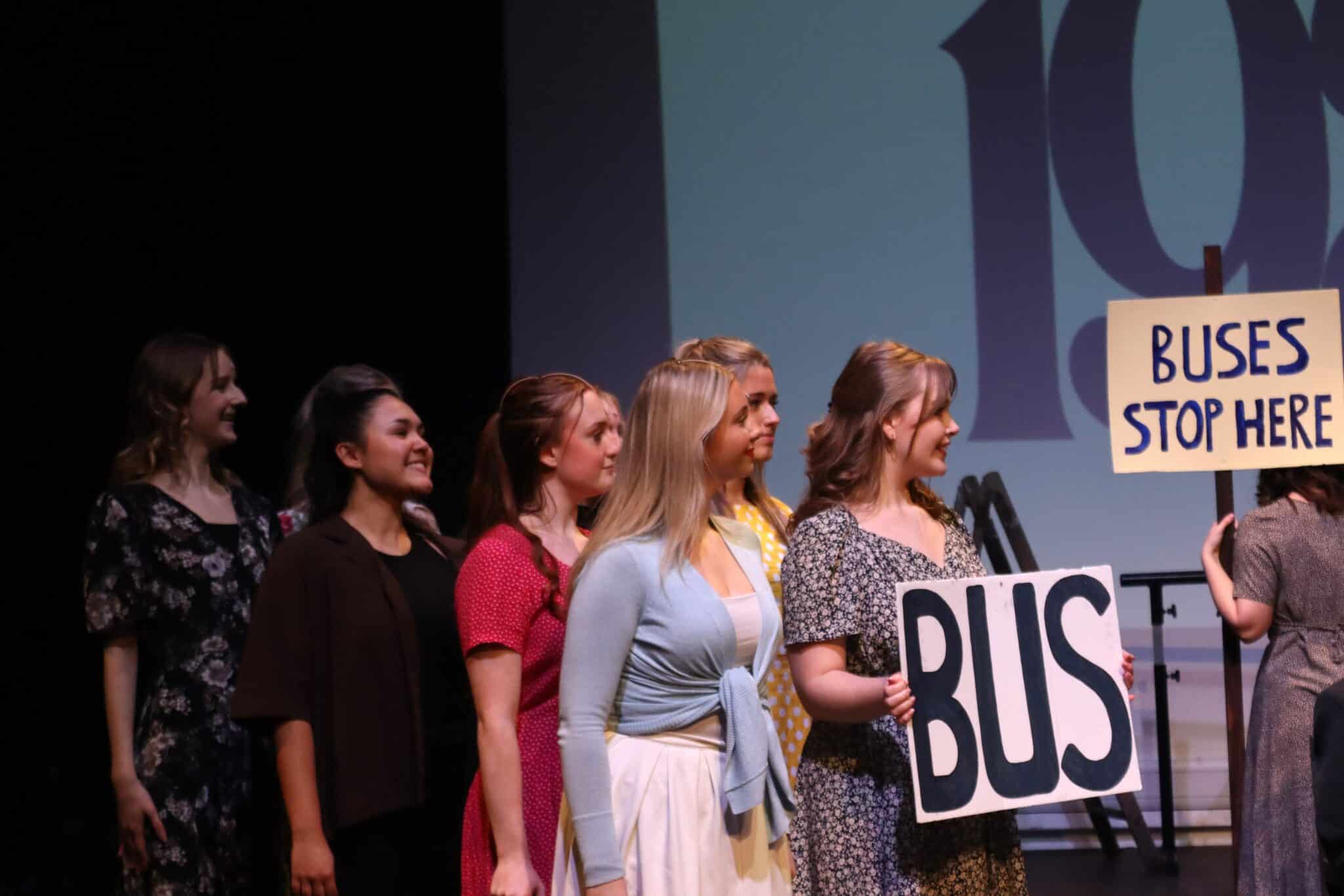 People on stage holding a bus sign