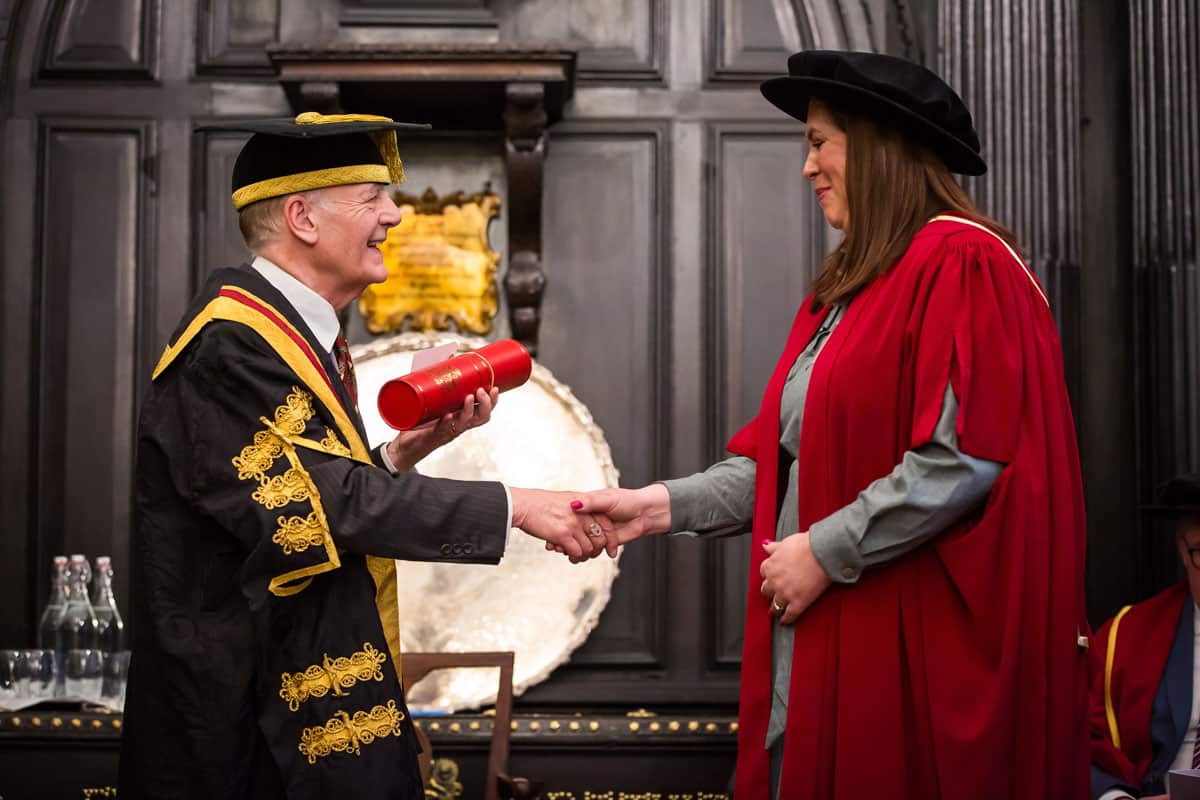 Two people in graduation gowns shaking hands